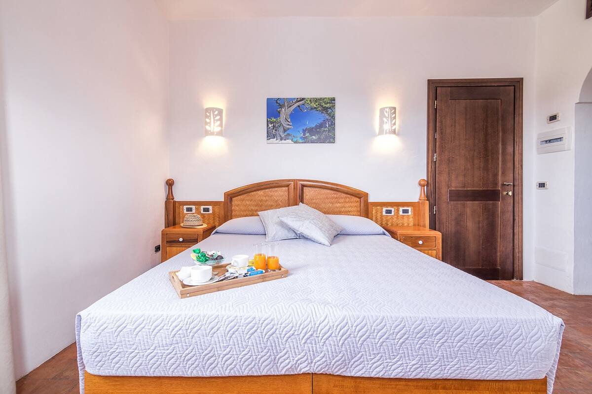 A neatly made bed with a white quilt, a tray with breakfast items, and a painting on the wall.