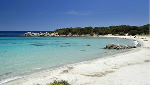 Uma praia com águas turquesa cristalinas, areia branca e afloramentos rochosos.