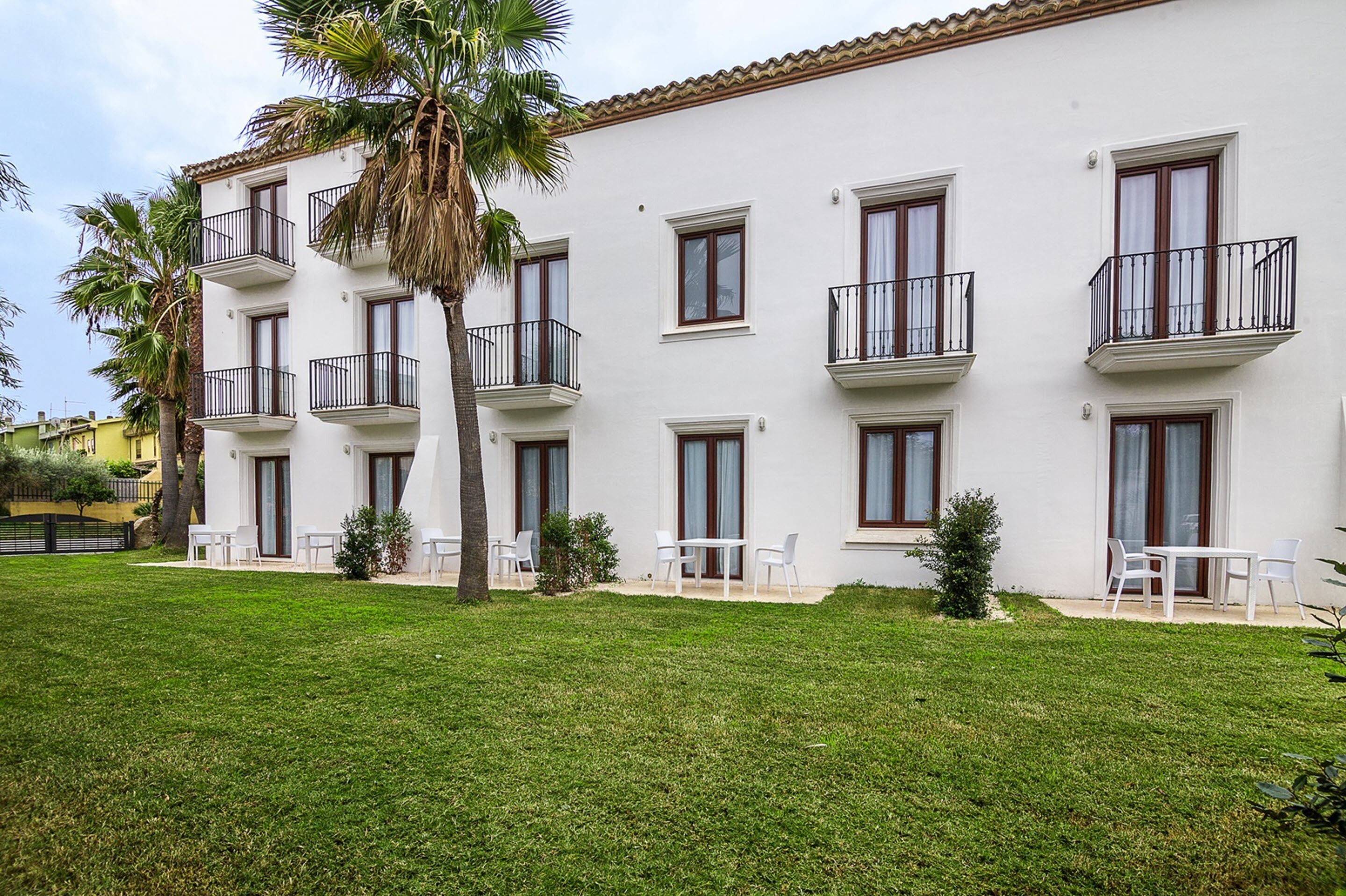 A white building with balconies, a lawn, and white furniture.