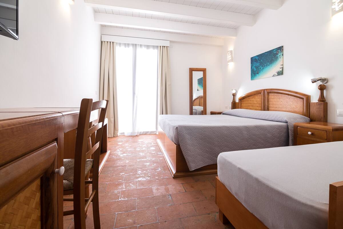 A hotel room with two beds, a wooden dresser, a chair, a mirror, and a painting on the wall.