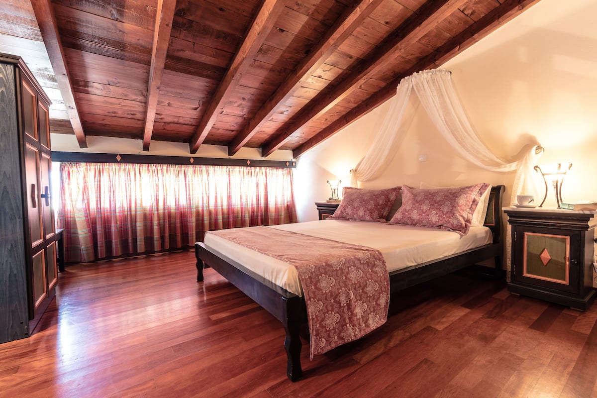 A bedroom with a wooden ceiling, a bed with a canopy, a nightstand, and a wardrobe.