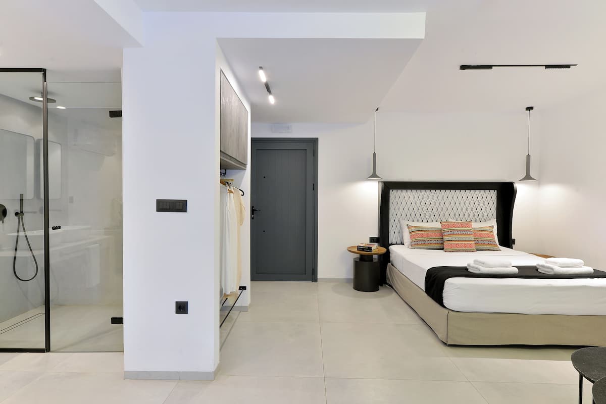 A modern bedroom with a bed, bedside table, and a glass-enclosed shower area.
