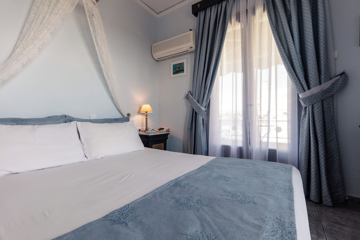 A neatly made bed with a white and blue bedspread, a bedside lamp, and a wall-mounted air conditioner.