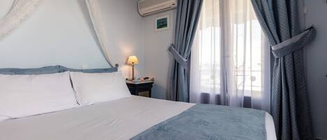 Una cama bien tendida con una colcha blanca y azul, una lámpara de noche y un aire acondicionado montado en la pared.