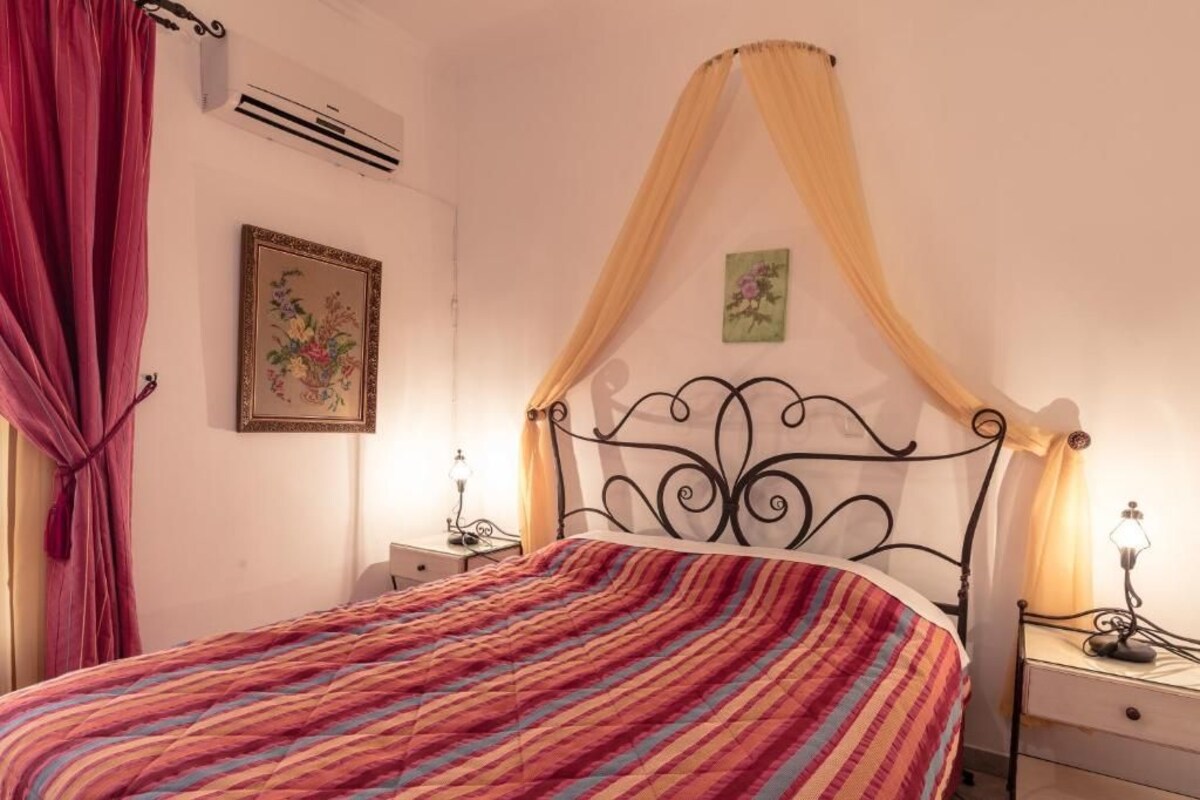 A bed with a striped bedspread, a canopy, a bedside table with a lamp, and a wall-mounted air conditioner.