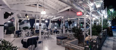 An outdoor restaurant with white furniture, hanging lights, and a stone wall.