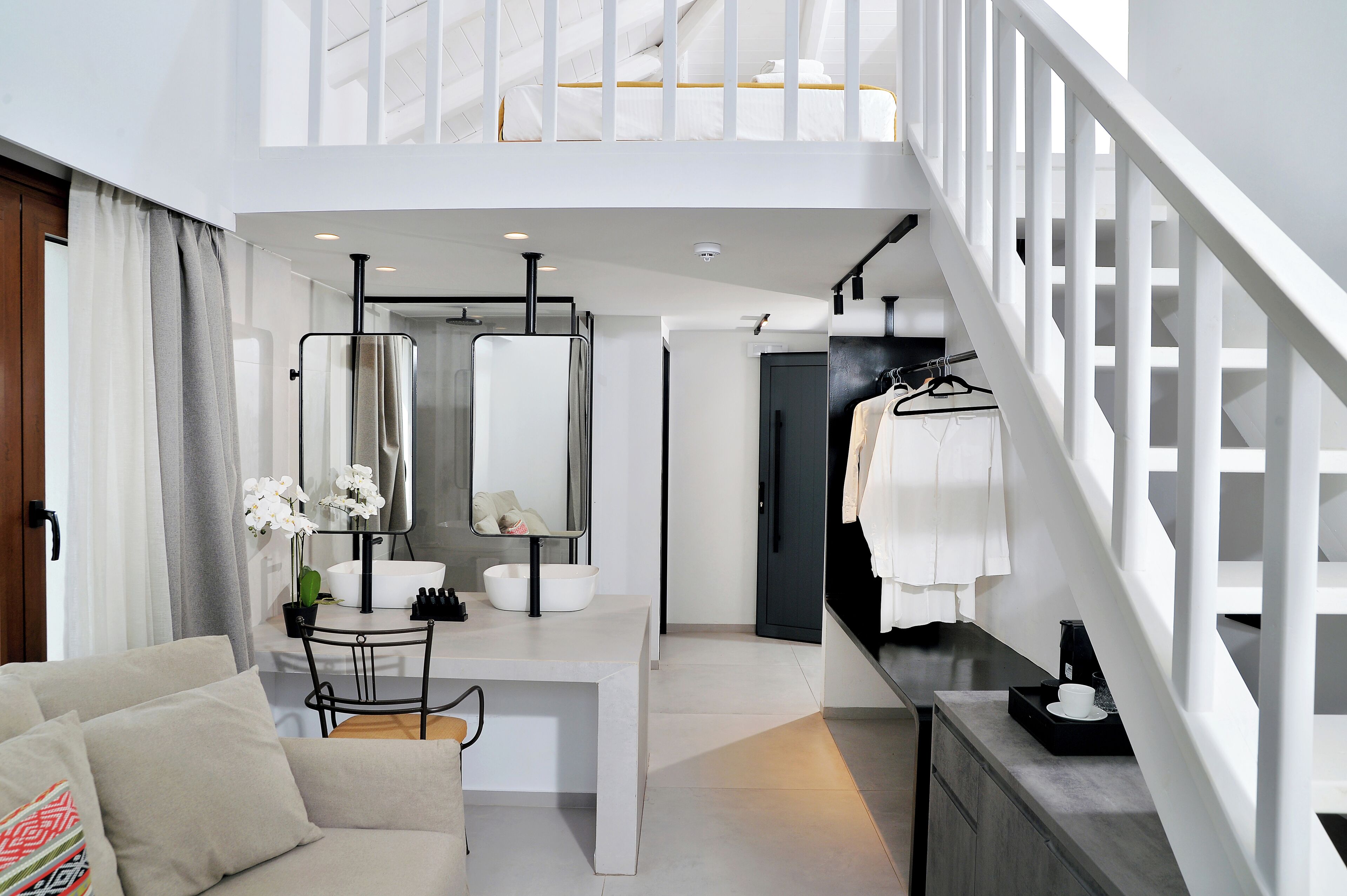 A modern hotel room with a dining area, a staircase, and a view of the city.