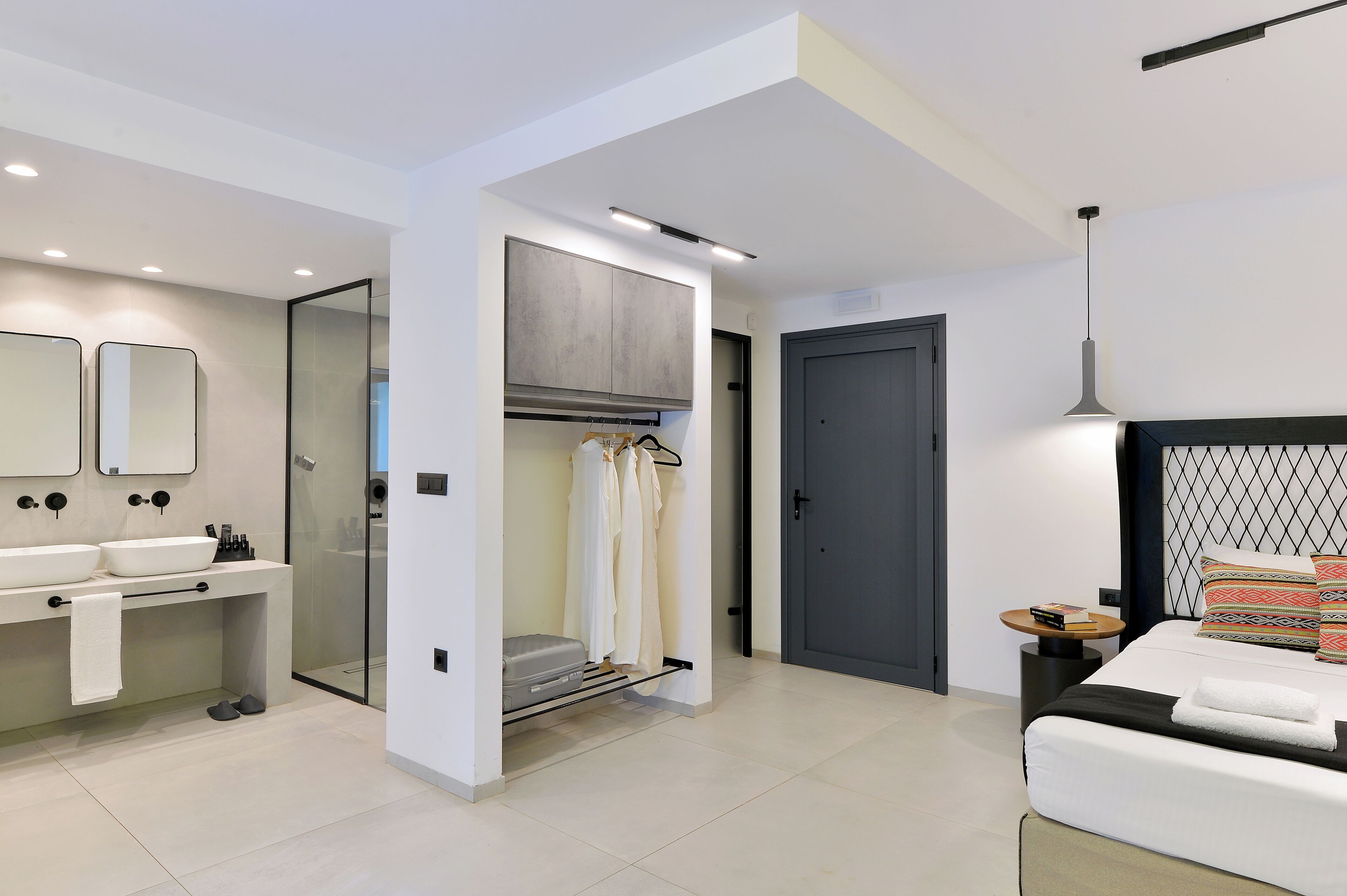 A modern hotel room with a large bed, a separate bathroom with a glass shower, and a walk-in closet.