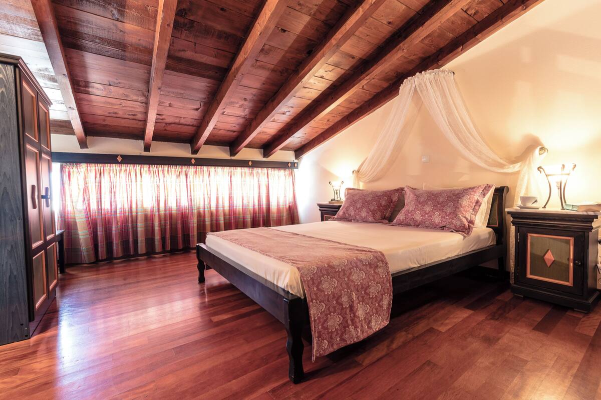 A bedroom with a wooden ceiling, a bed with a canopy, a nightstand, and a wardrobe.