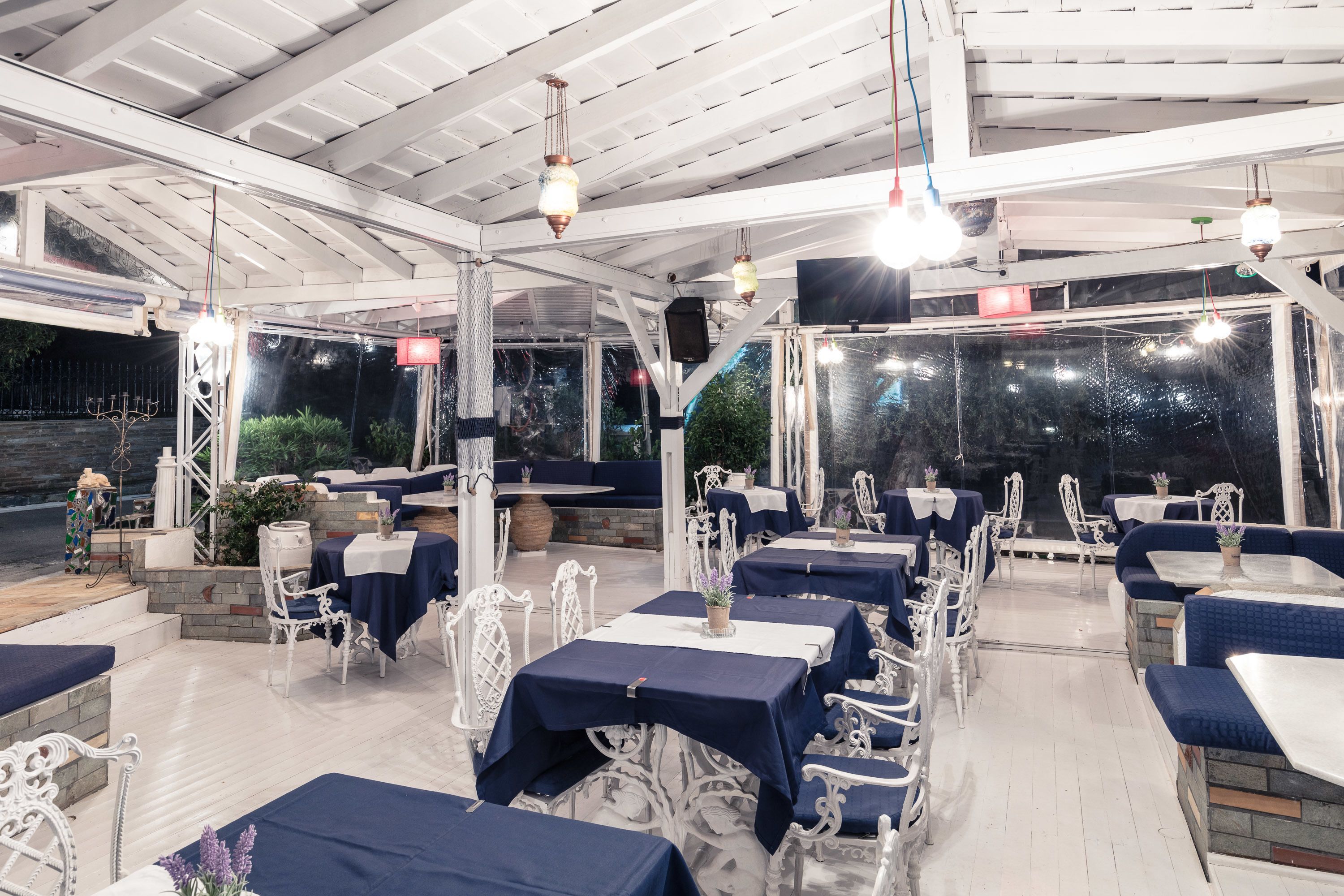 Un área de comedor al aire libre con mobiliario metálico blanco y mesas cubiertas con manteles azules.