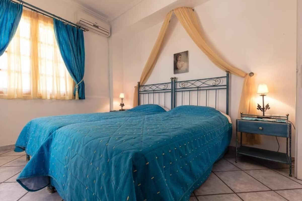 A bedroom with a bed, curtains, a nightstand, a lamp, and a painting on the wall.