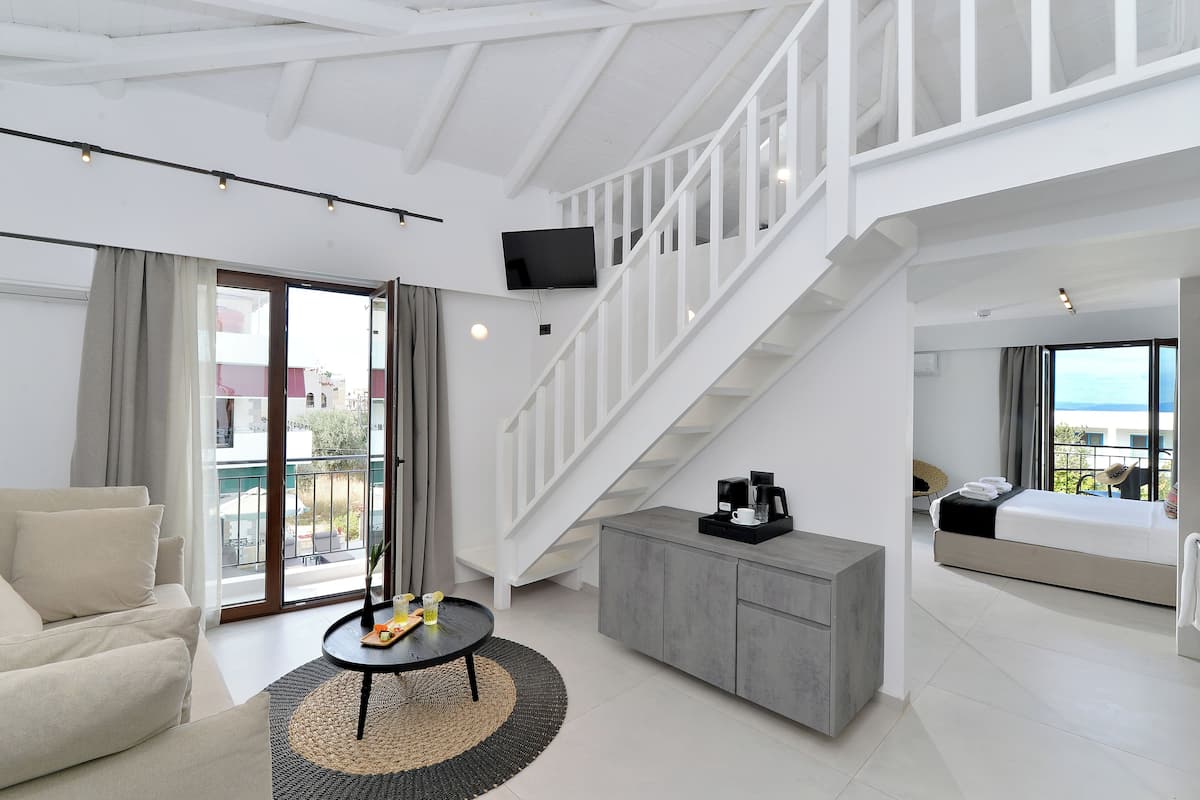 A modern hotel room with a balcony, a staircase, a sofa, a coffee table, and a bed.