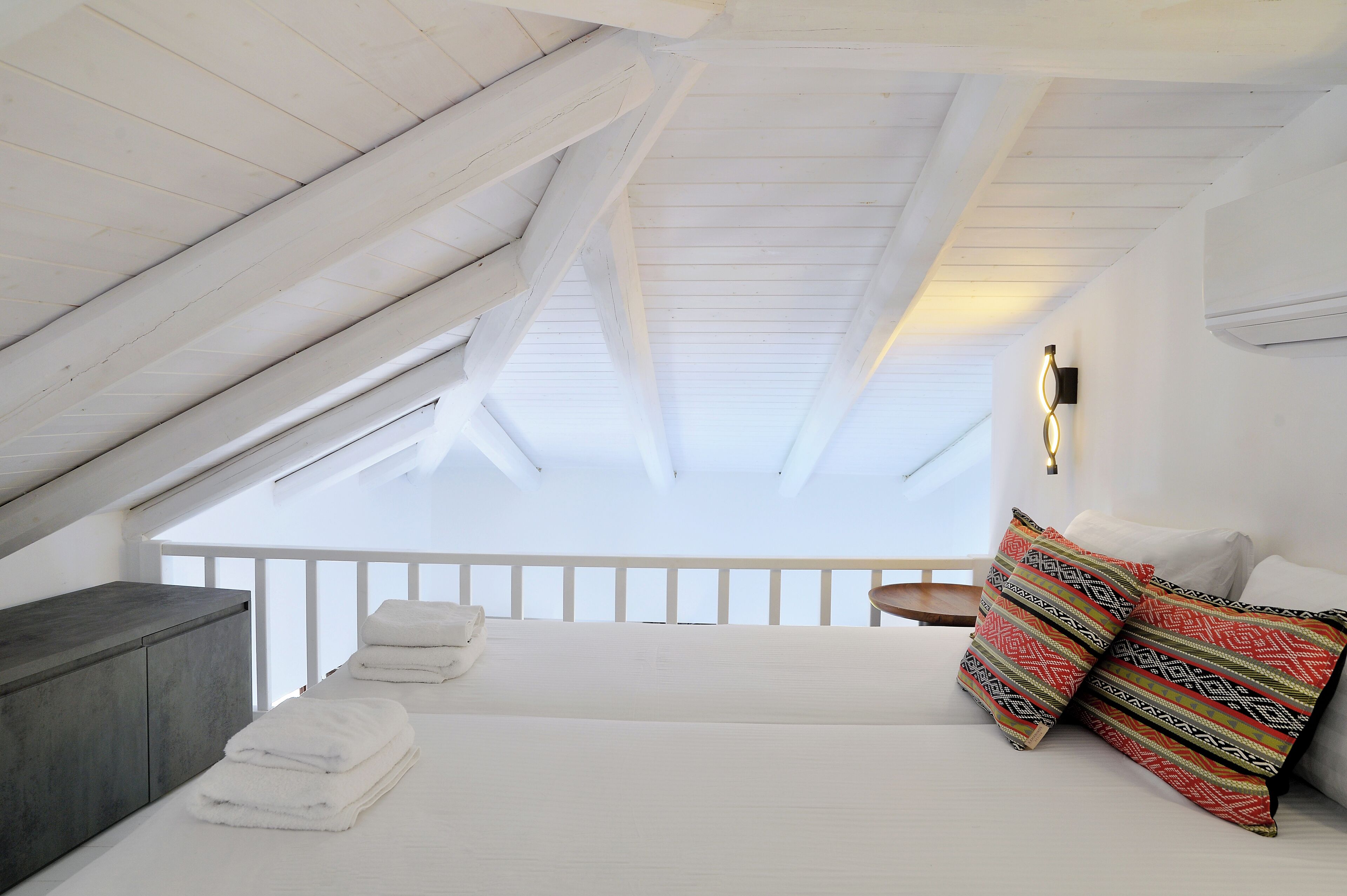 Ein Schlafzimmer mit schrägem Dach, einem Bett mit gemusterten Kissen, einem Nachttisch und einem Beistelltisch.