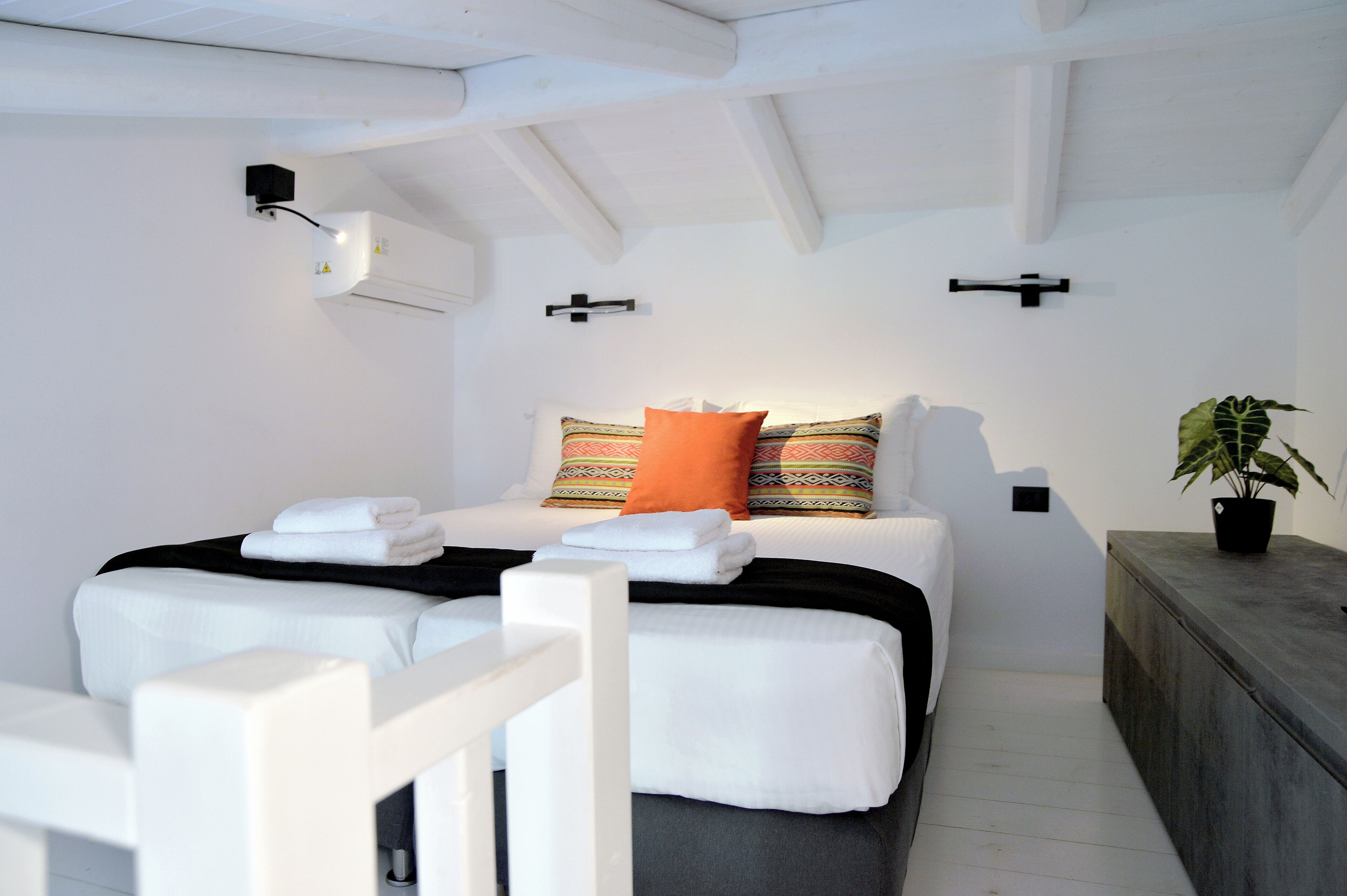 Een moderne slaapkamer met een bed, kussens en een nachtkastje met een plant.