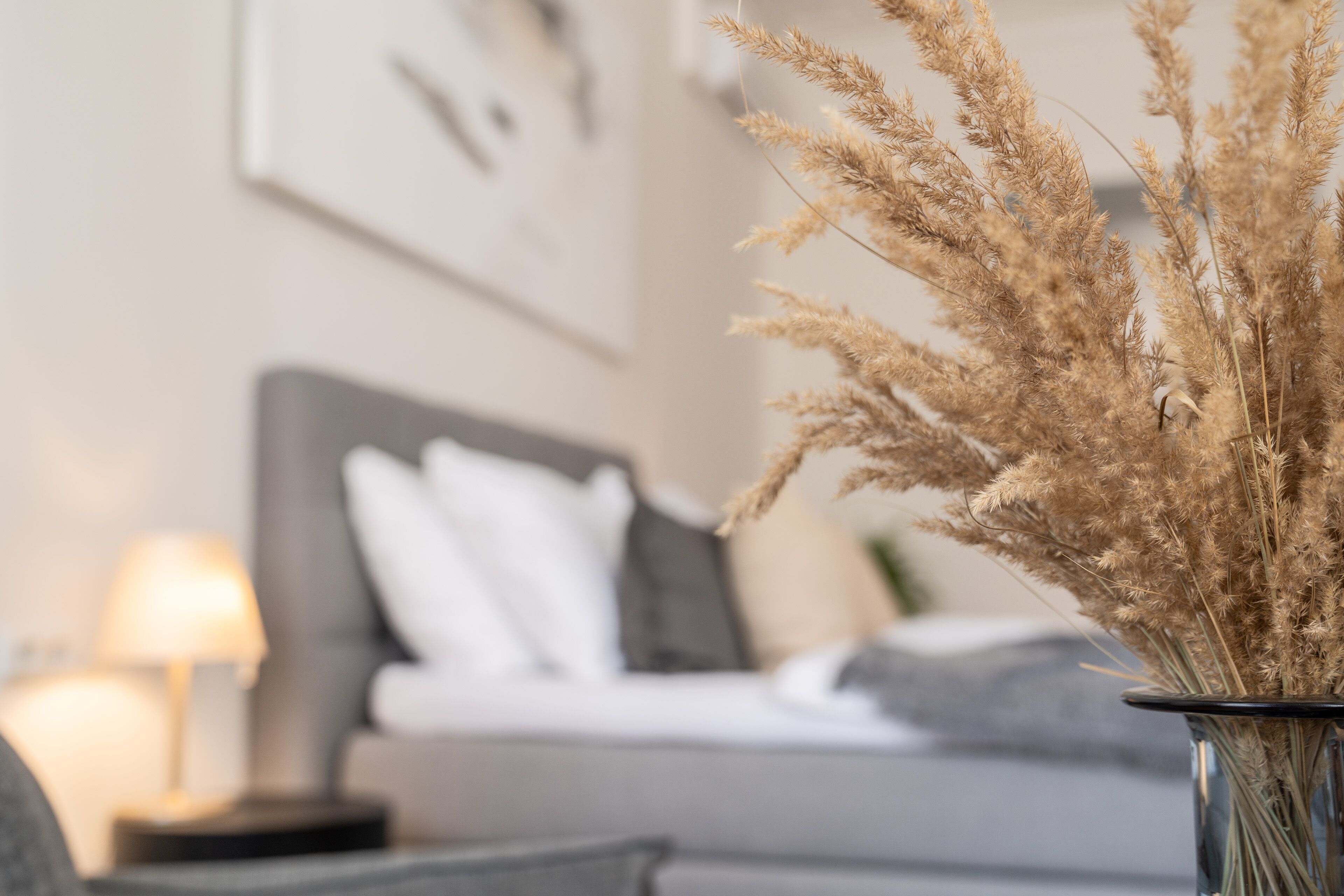 A living room with a sofa, a lamp, and a vase with dried plants.