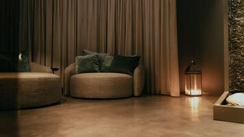 A cozy living room with a round beige sofa, a smaller armchair, and a floor lamp.