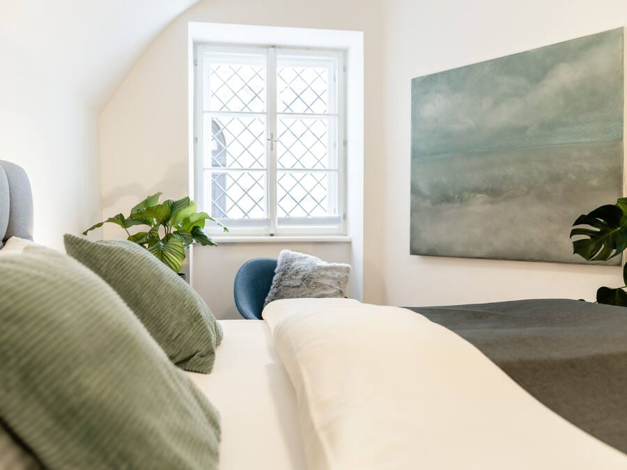 A bedroom with a bed, a window, a painting, and a chair.