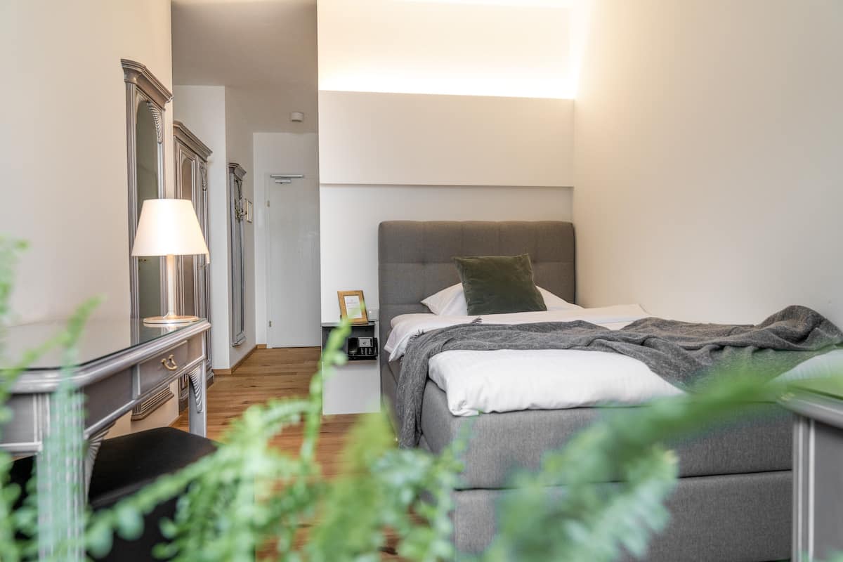 Un dormitorio con cama, mesita de noche, lámpara y espejo.
