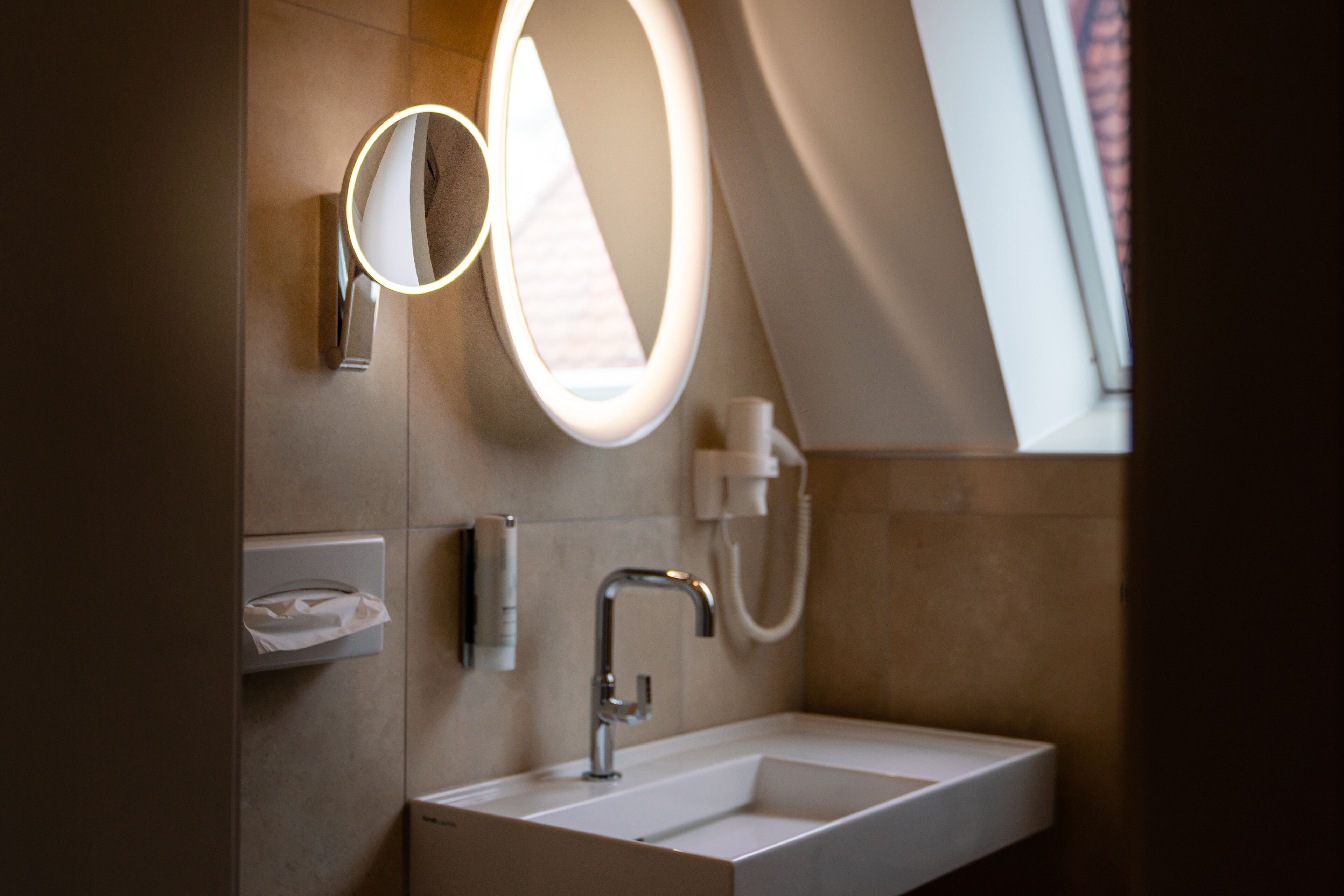 A modern bathroom with a large mirror, a sink, and a towel dispenser.