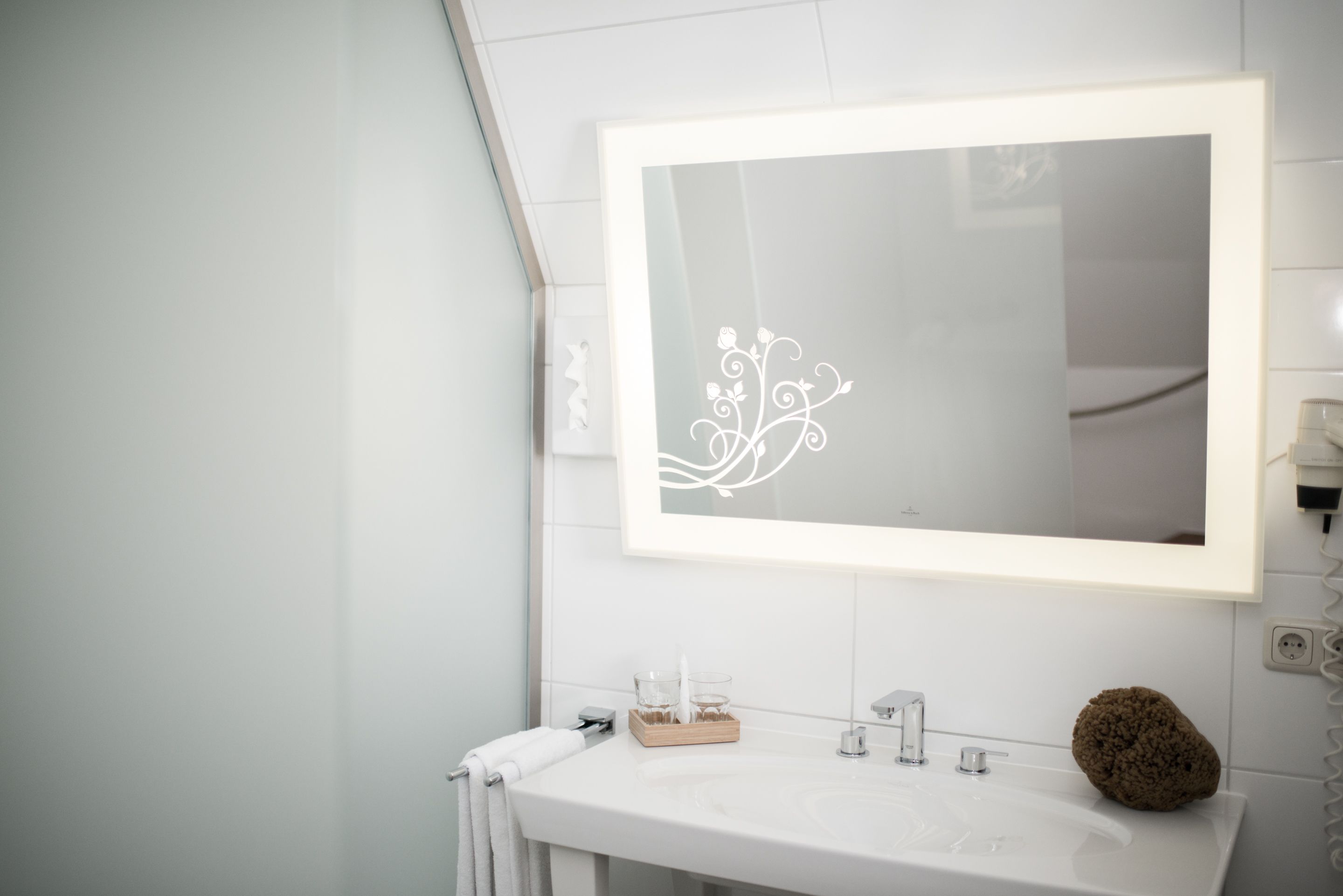A bathroom with a white sink, a mirror with a floral design, and a towel rack.