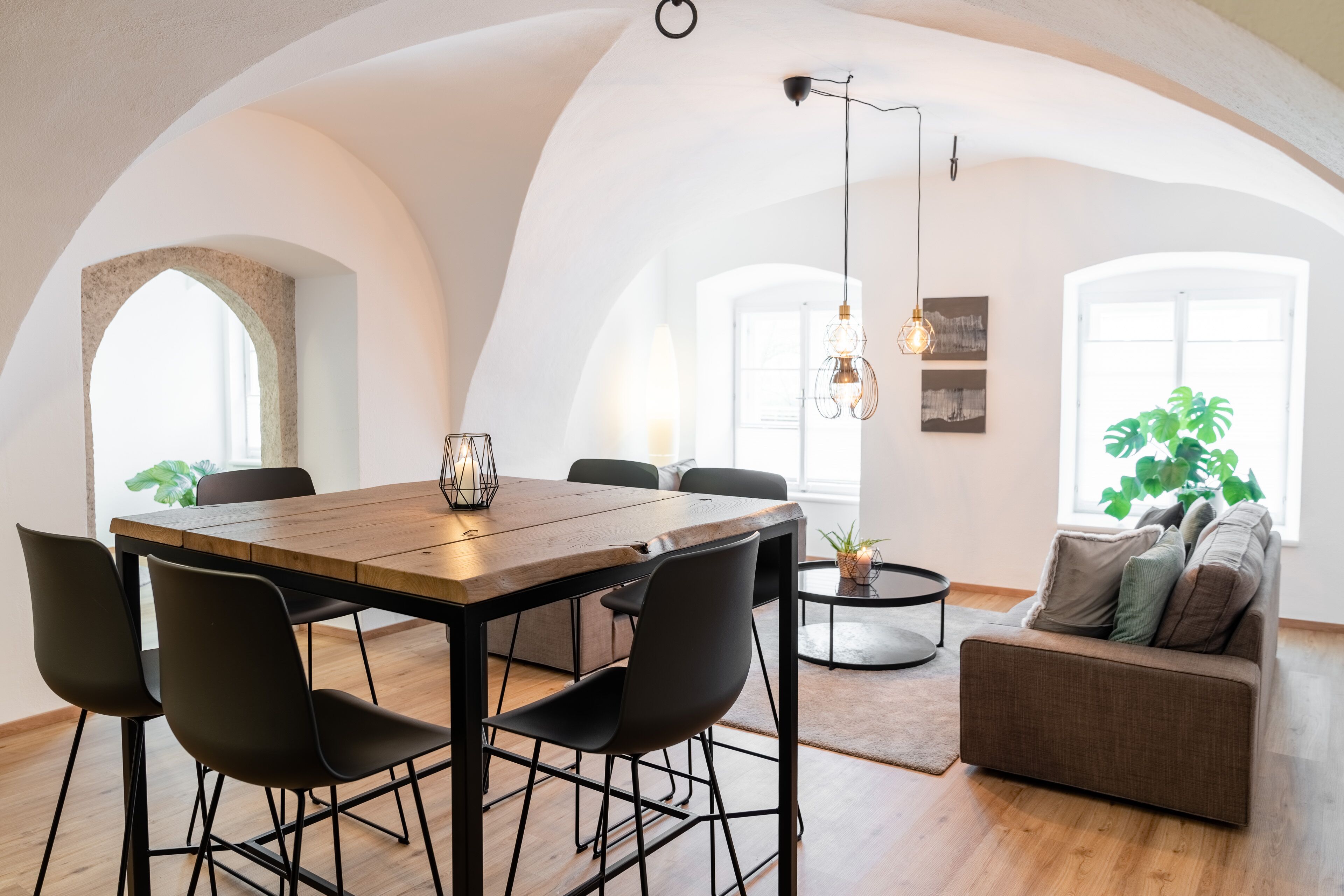 Un coin repas avec une table en bois et des chaises noires, un canapé et un luminaire suspendu.