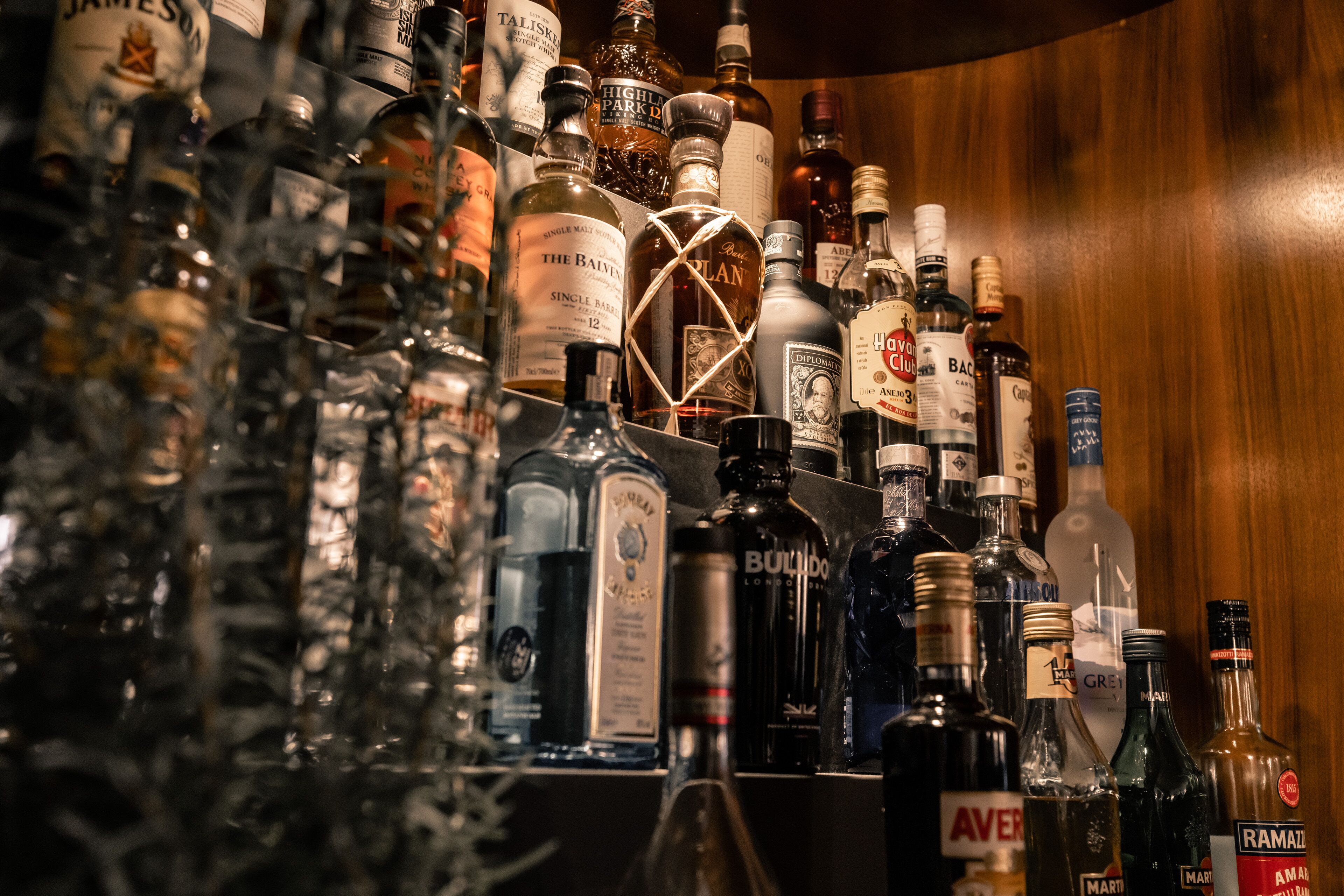 Una zona de bar con varias botellas de alcohol, incluyendo whisky y vodka, dispuestas en estanterías.