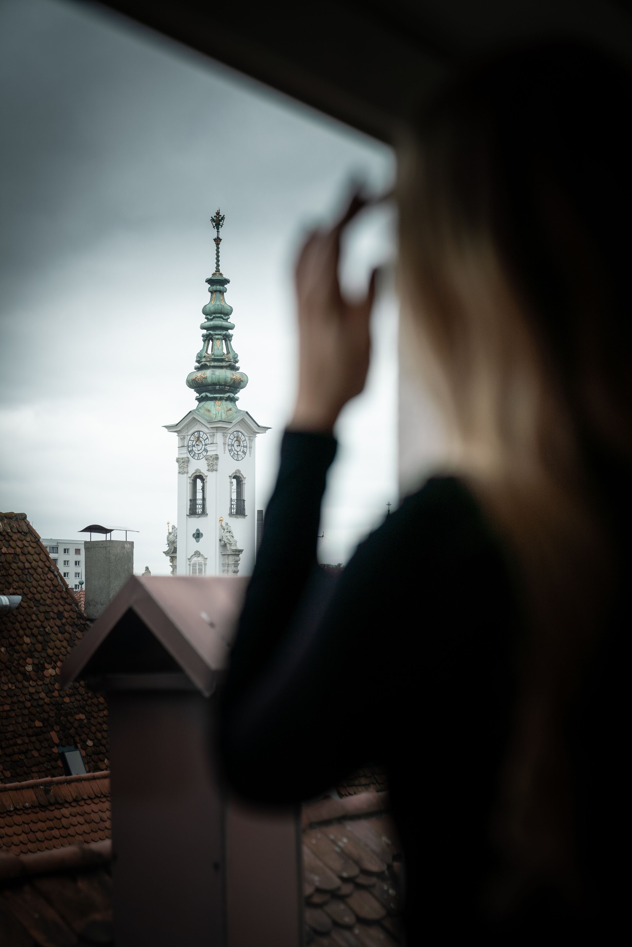 A person looking out from a window at a building with a clock tower.