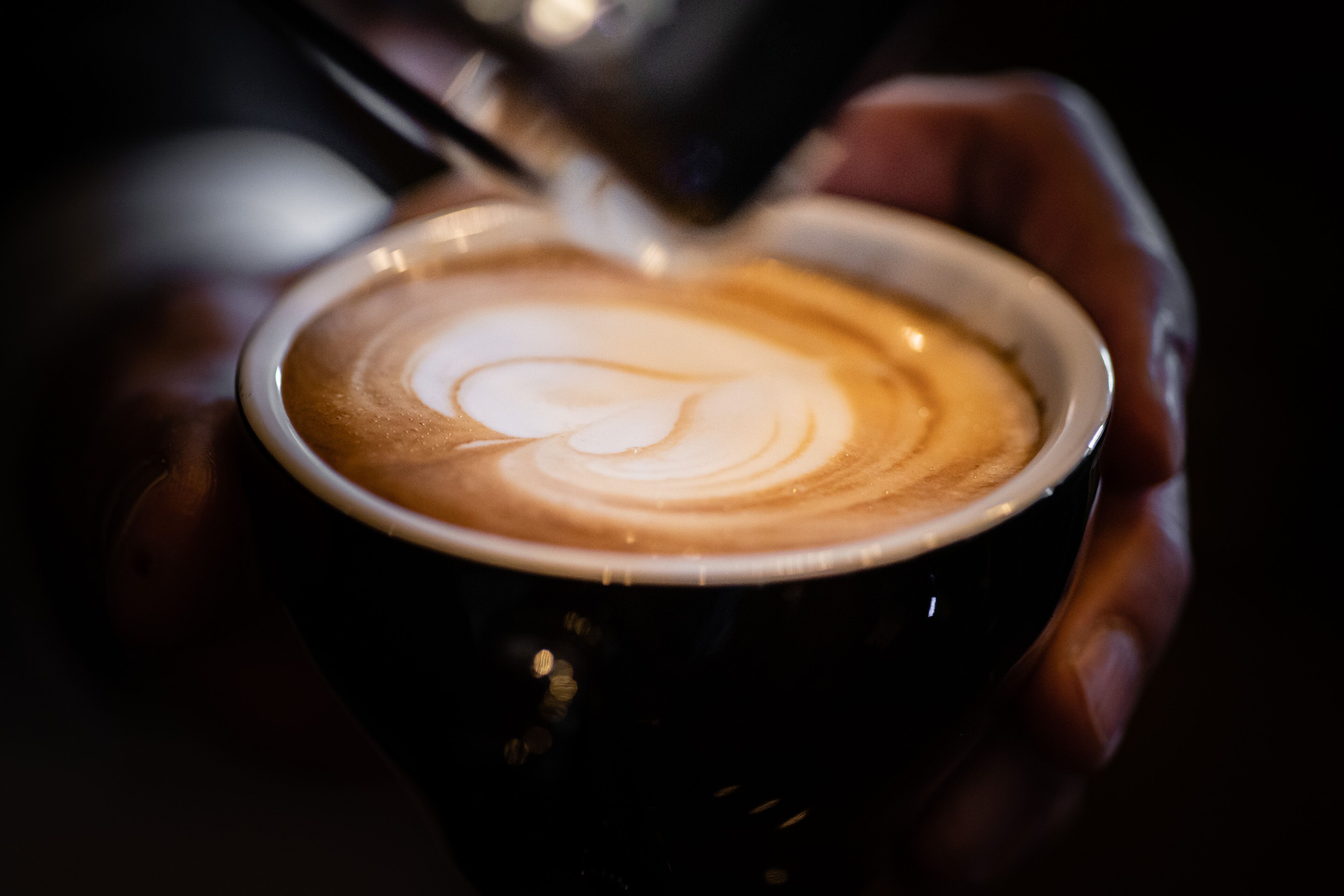 A close-up of a hand holding a cup of coffee with latte art.