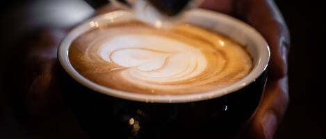 A close-up of a hand holding a cup of coffee with latte art.