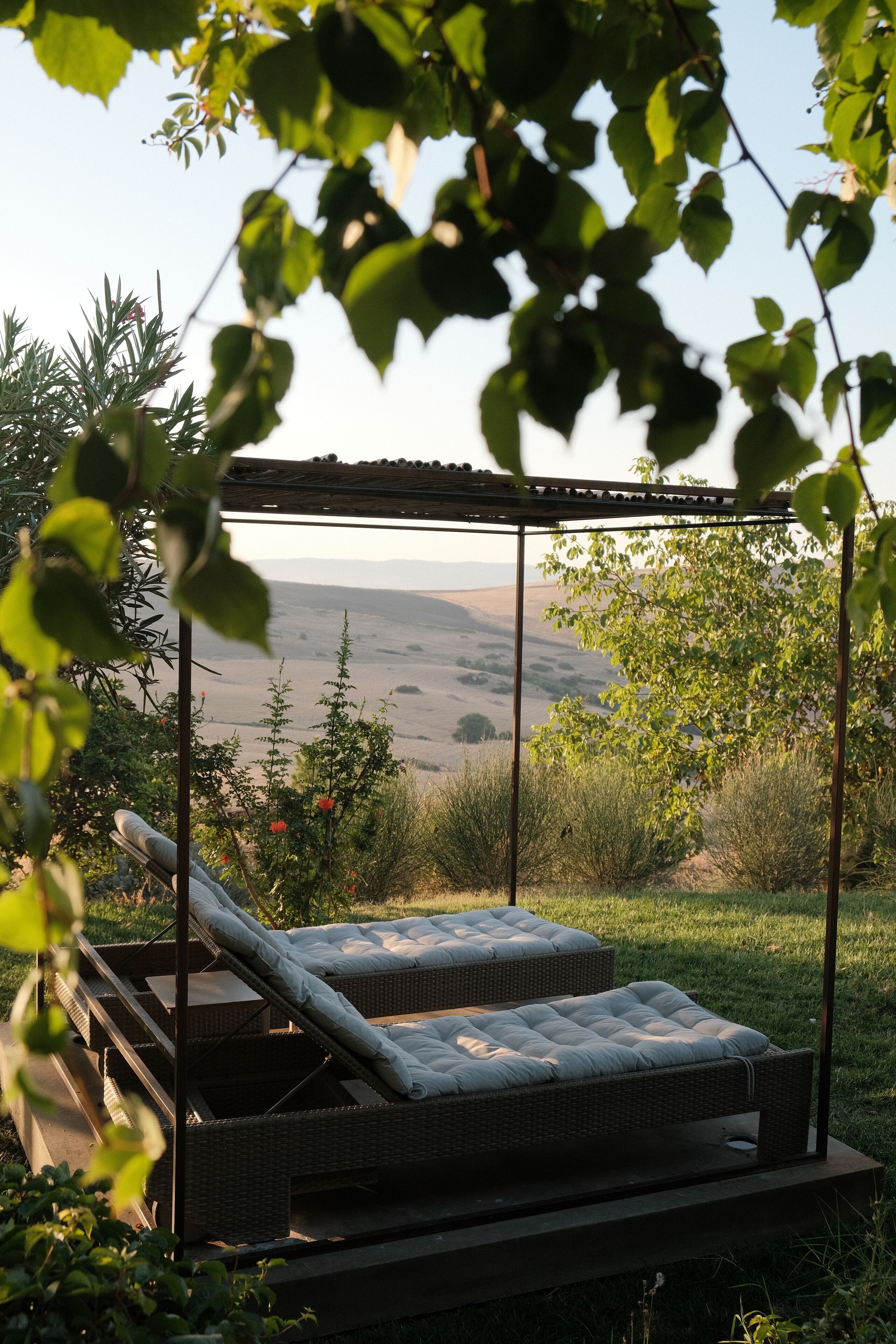 A covered outdoor seating area with two cushioned benches and a pergola structure.