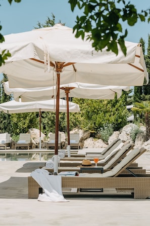 A poolside area with lounge chairs and umbrellas. - Masseria Susafa (Polizzi Generosa)