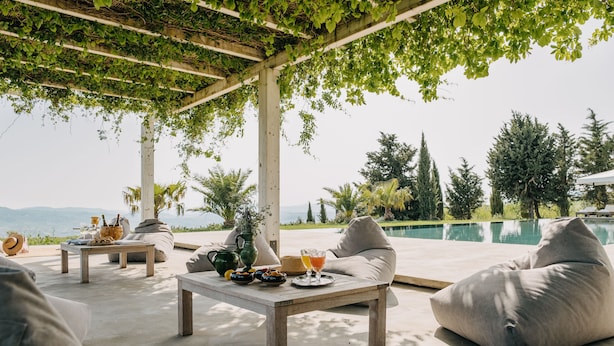Uma área externa com assentos, piscina, mobiliário acolchoado e uma mesa com bebidas e petiscos.