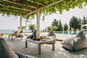 Un espacio al aire libre con piscina, asientos acolchados y una mesa con bebidas y aperitivos.