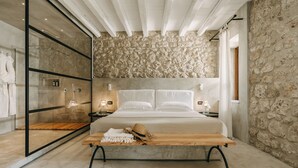 Quarto moderno com parede de pedra, uma cama grande, um banco de madeira e um box de vidro.