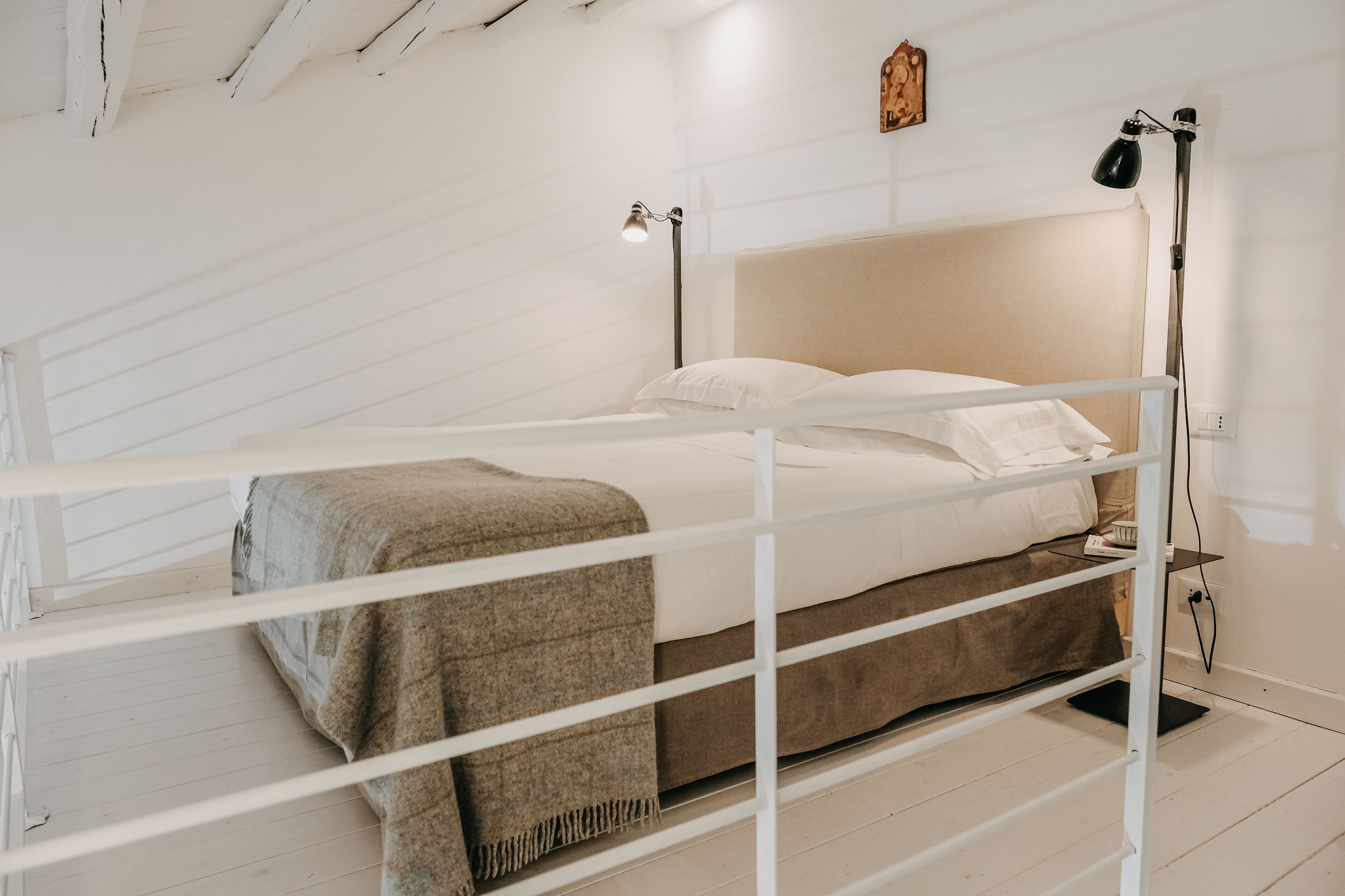 A bunk bed with a white frame, a beige headboard, and a brown blanket. There is a bedside table with a lamp and a power outlet.