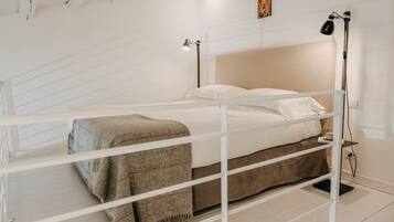 A bunk bed with a white frame, a beige headboard, and a brown blanket. There is a bedside table with a lamp and a power outlet.