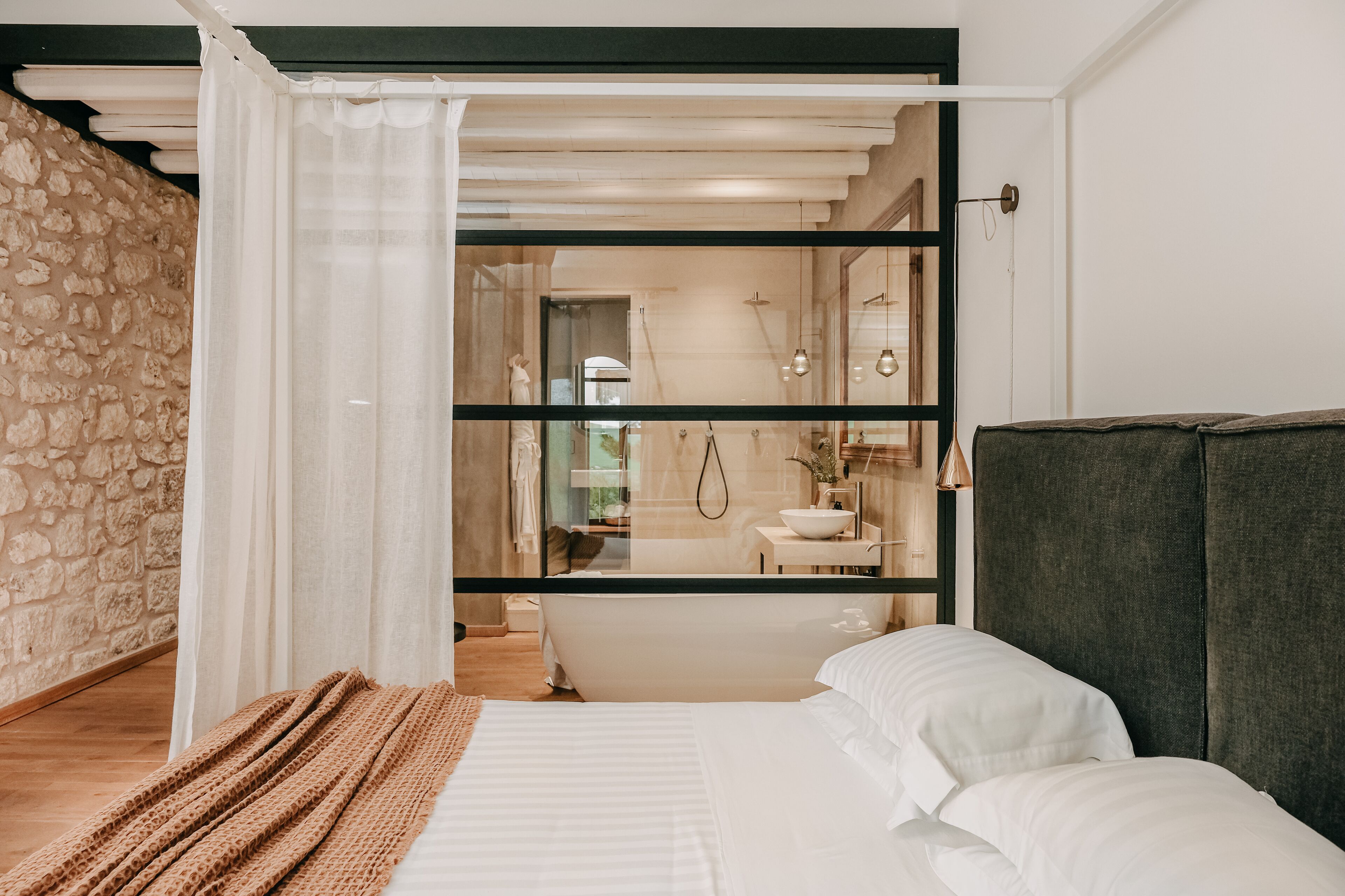 Una camera da letto moderna con un letto grande, una testata scura e vista su un bagno tramite una porta di vetro.
