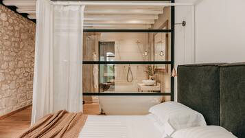 Una camera da letto moderna con un letto grande, una testata scura e vista su un bagno tramite una porta di vetro.