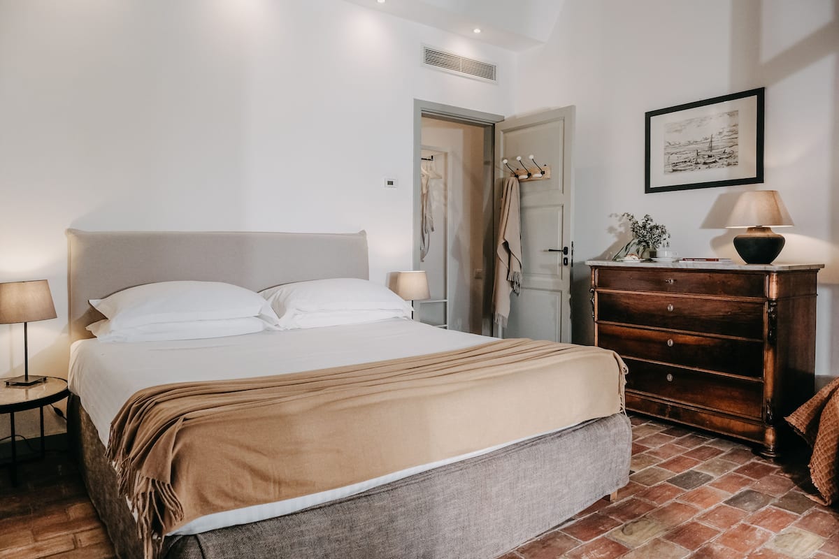 A neatly arranged bedroom with a bed, bedside tables, a dresser, and a framed picture on the wall.