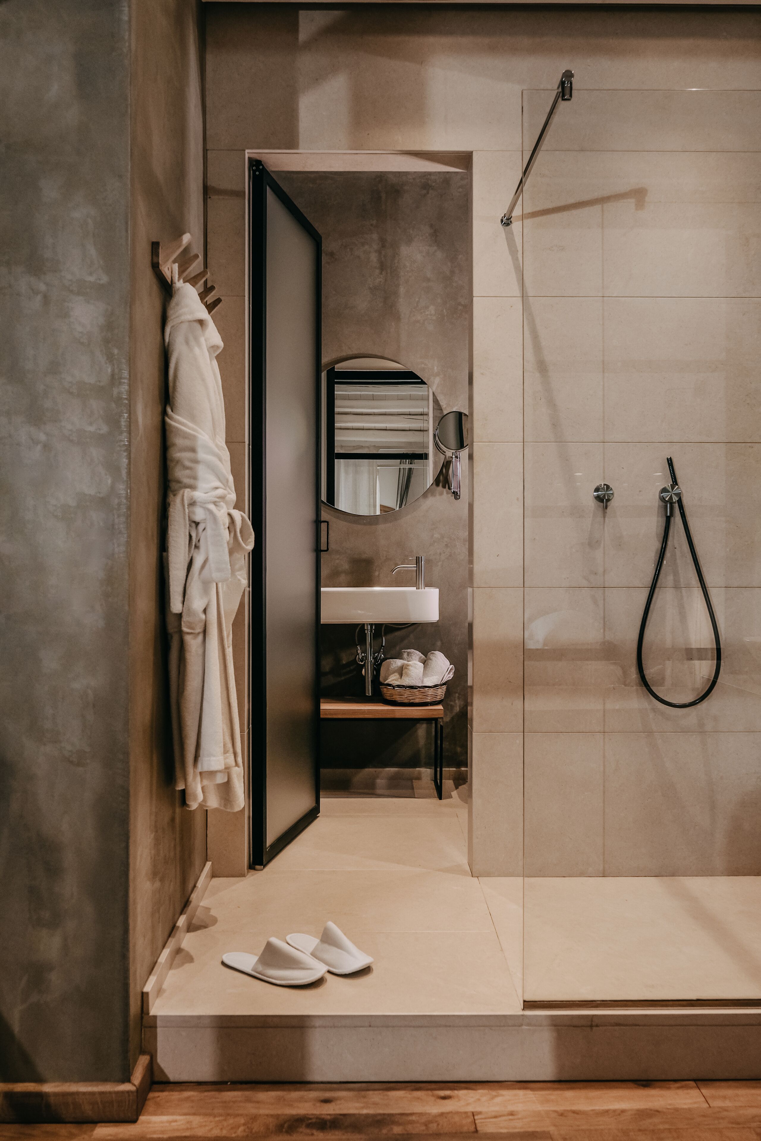 Ein modernes Badezimmer mit Bodendusche, einem Bademantel auf einem Haken, einem Waschbecken mit Spiegel und einem Tablett mit Pflegeprodukten.