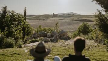 Una persona con sombrero sentada en una colina con hierba, contemplando campos en terrazas.