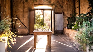 Quarto rústico com uma mesa de madeira, parede de pedra e uma janela com luz solar entrando.