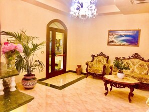 Un hall d’entrée avec un sol en marbre, un lustre, un canapé, une table ornée d’une plante et un tableau accroché au mur.