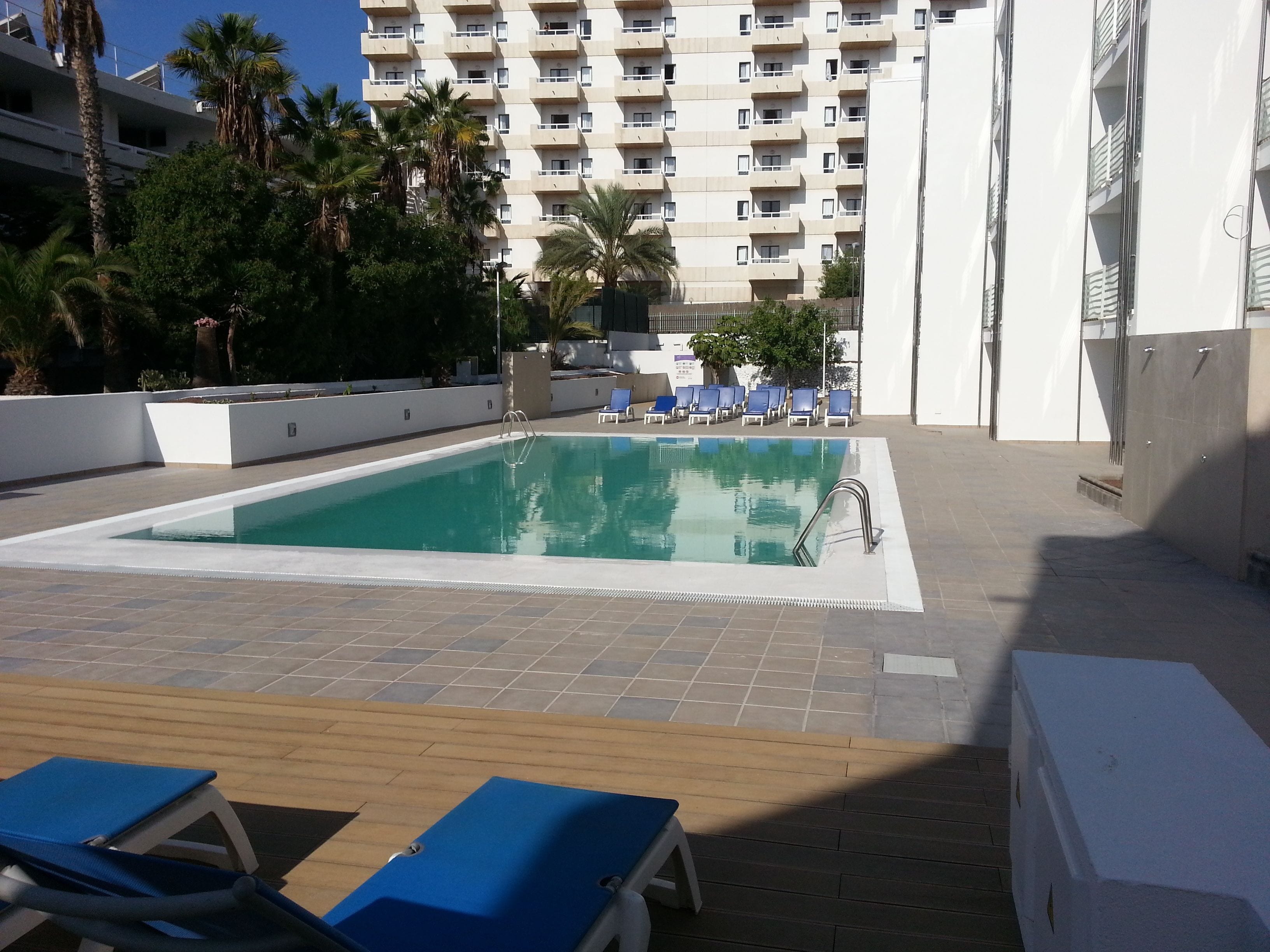 A swimming pool with lounge chairs and a high-rise building in the background.