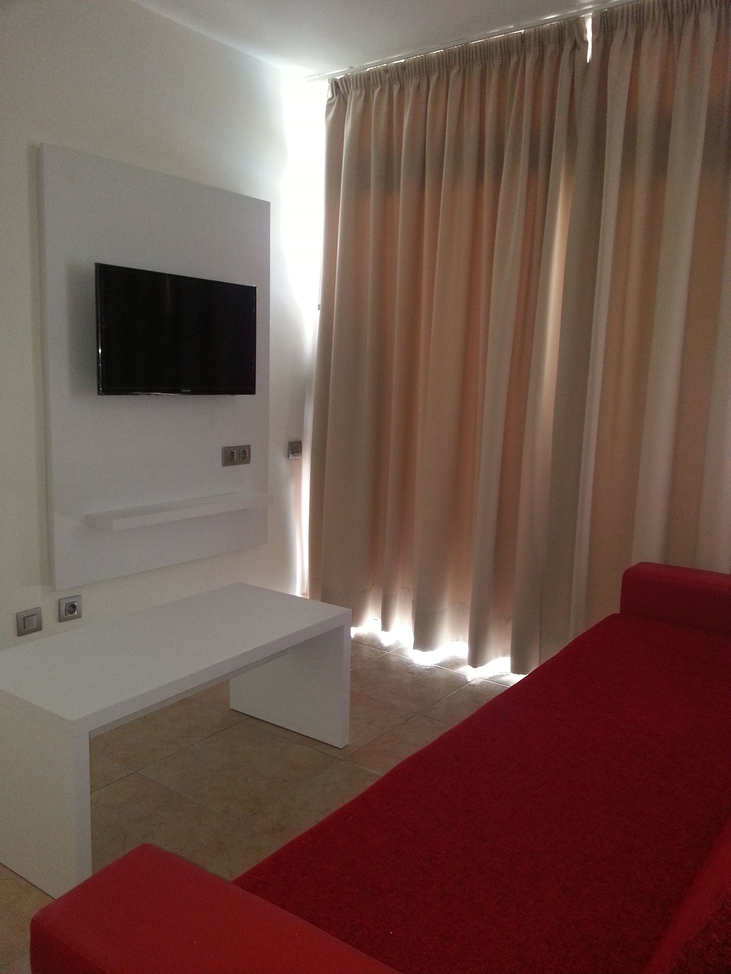 A modern living room with a flat-screen TV mounted on a white wall, a red sofa, and a beige carpet.