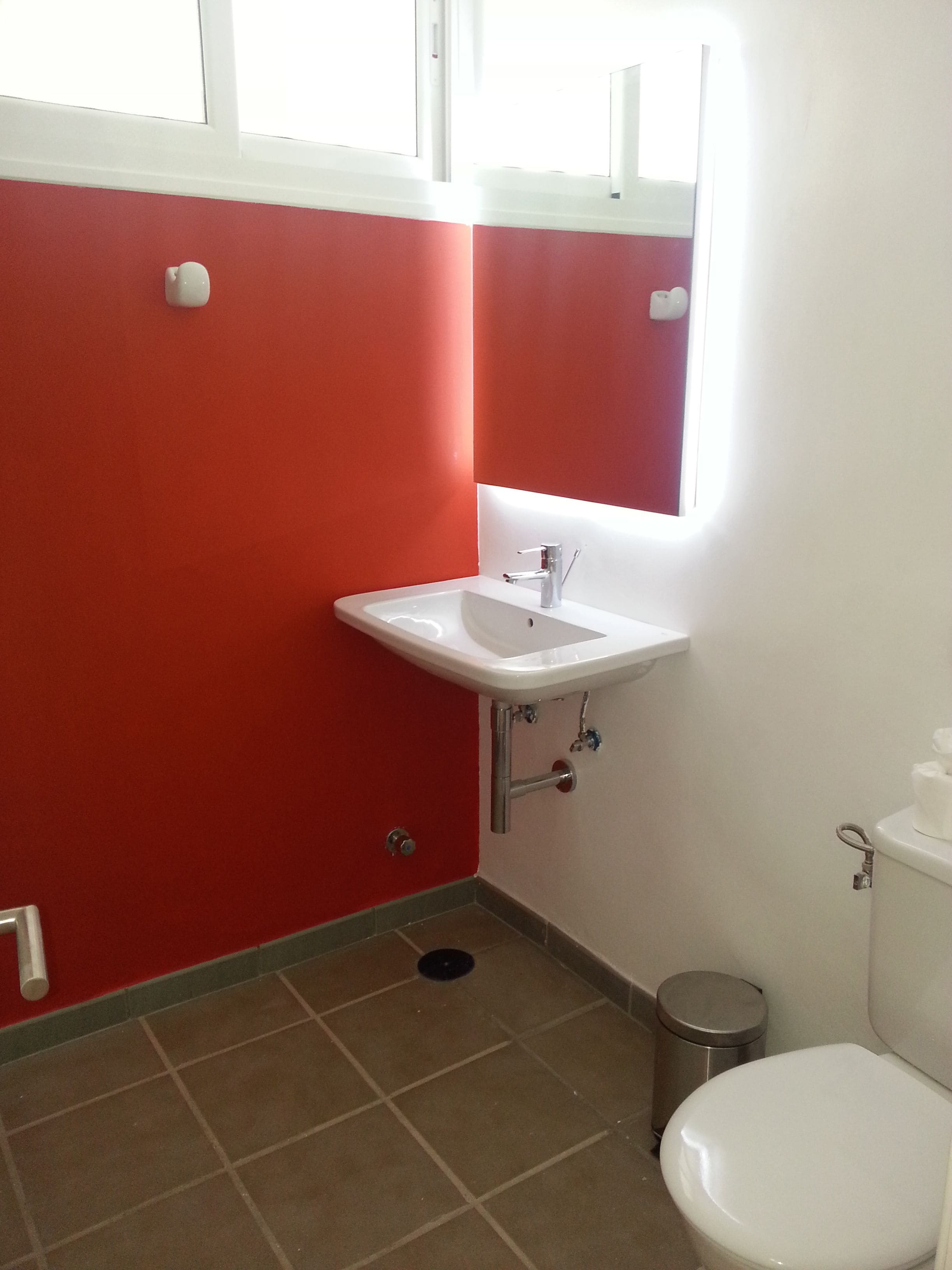 Une petite salle de bain avec un lavabo blanc, des murs rouges et des toilettes blanches.