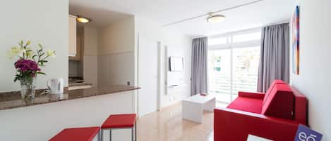 Une chambre d’hôtel moderne dotée d’un coin cuisine, d’un canapé rouge, d’une petite table avec un téléphone et d’une enseigne indiquant le nom de l’hôtel.