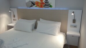 Un lit bien fait, avec du linge de lit blanc, une œuvre d’art représentant des rochers et une fleur, accrochée au mur, et deux lampes de chevet.