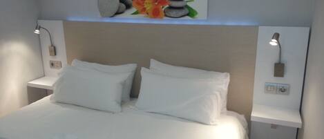 A neatly made bed with white linens, a wall-mounted artwork of rocks and a flower, and two bedside lamps.