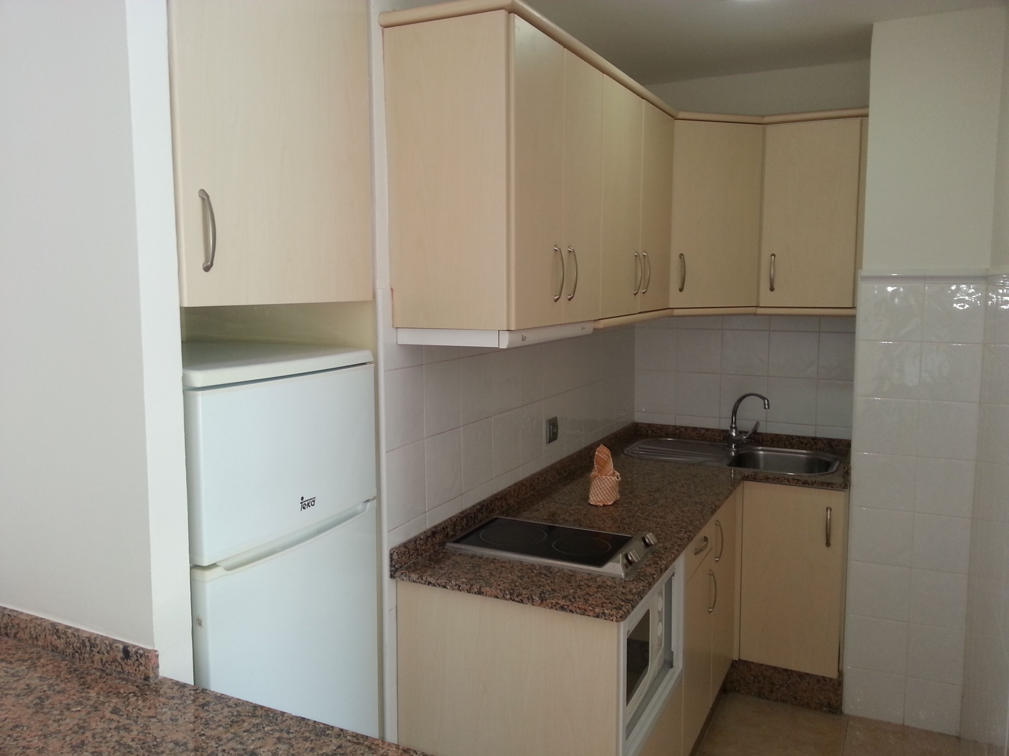 A compact kitchen with white cabinets, a built-in oven, a sink, and granite countertops.